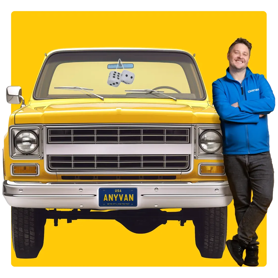 Smiling man in a blue AnyVan jacket leaning on a bright yellow vintage car with a fuzzy dice rearview mirror and custom plate that reads “ANYVAN,” set on a yellow background.